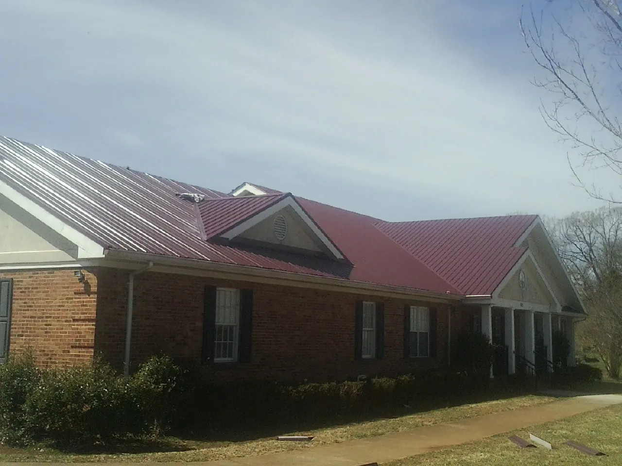 Red metal roof with gabled entries on a long brick building, from a Hail Damage Roof Repair job in Sebree