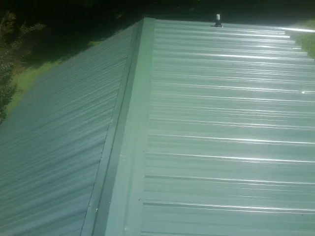 New green metal panels meeting at the ridge of a roof — Flat Roof Repair work by our crew in Sebree