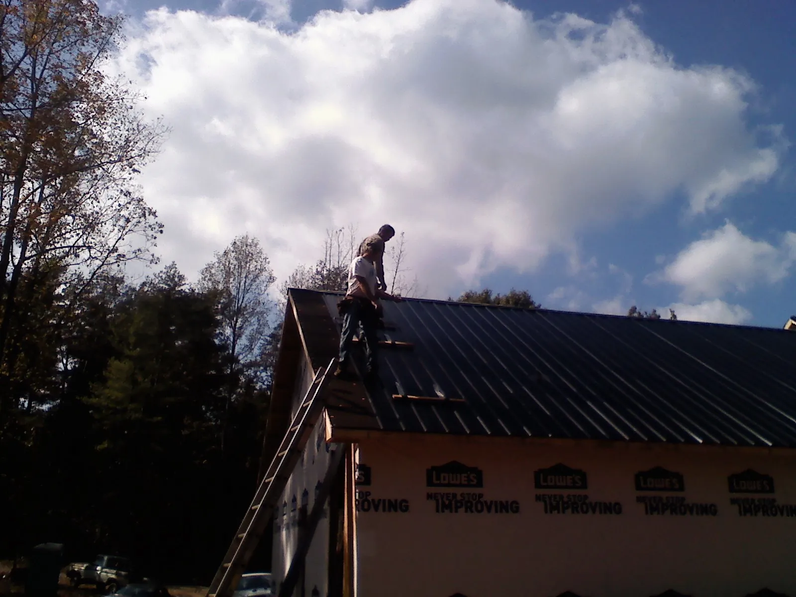 Roofer fastening dark metal panels high against a cloudy sky, from a Roof Inspection job in Sebree